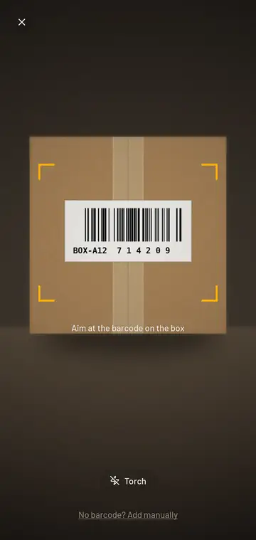 The scanner: a taped cardboard box with a barcode label, framed by four amber corner brackets, under the hint to aim at the barcode on the box.